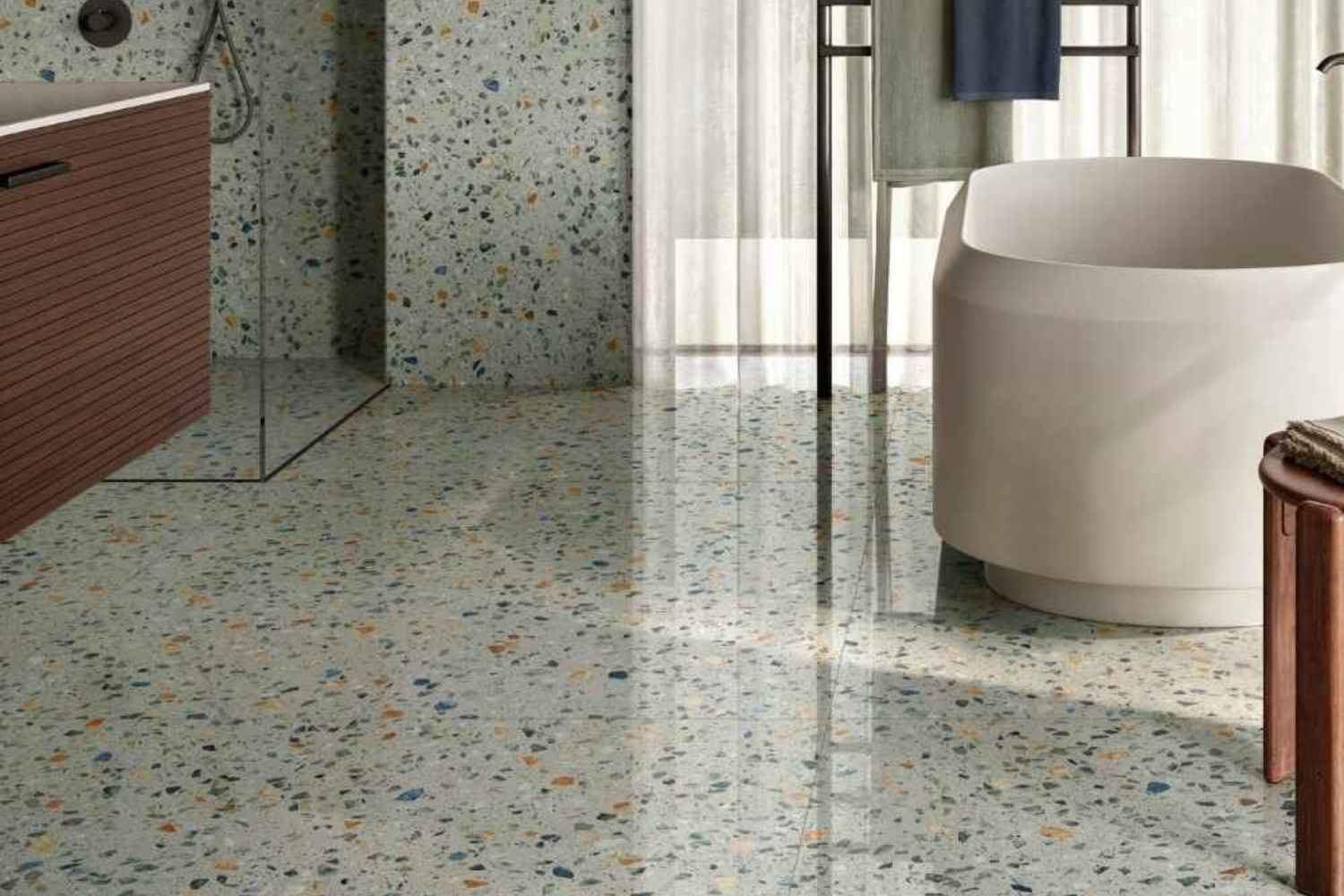 Sant Agostino Glow Plus Sage glänzend poliert als Boden- und Wandfliese in heller Terrazzo-Optik mit grünen, blauen und warmen Steineinschlüssen im modernen Badezimmer