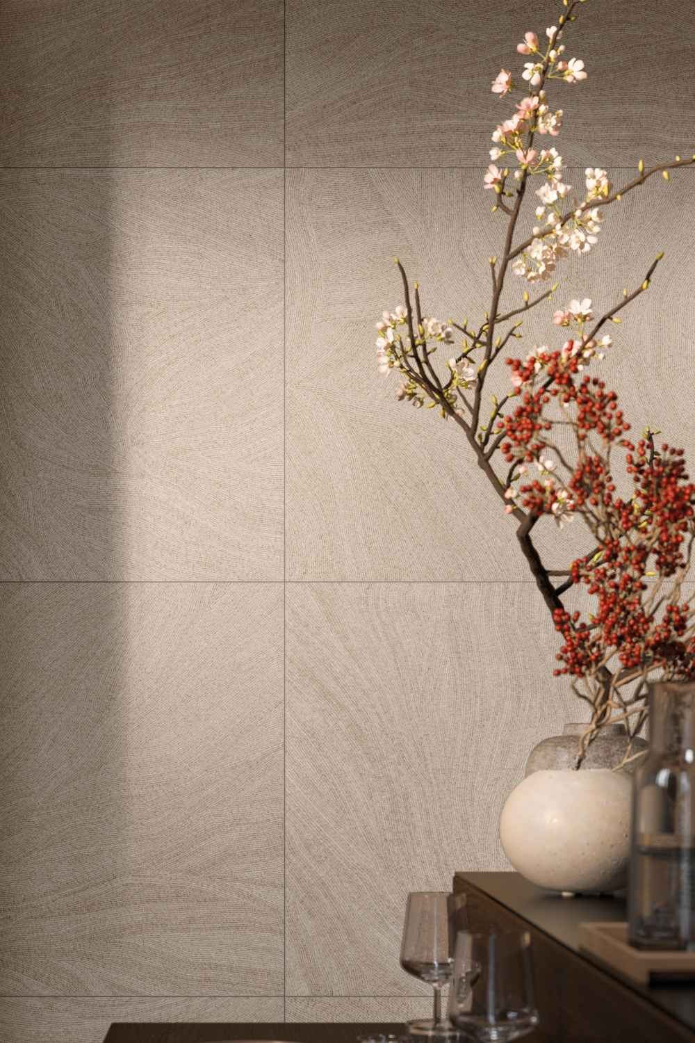 Refin Ink Cozy als Wandfliese in warmer Beige- und Taupe-Farbgebung mit feiner textilartiger Struktur und sanft geschwungenem Linienbild, dekoriert in einem modernen Wohnambiente mit floralen Akzenten