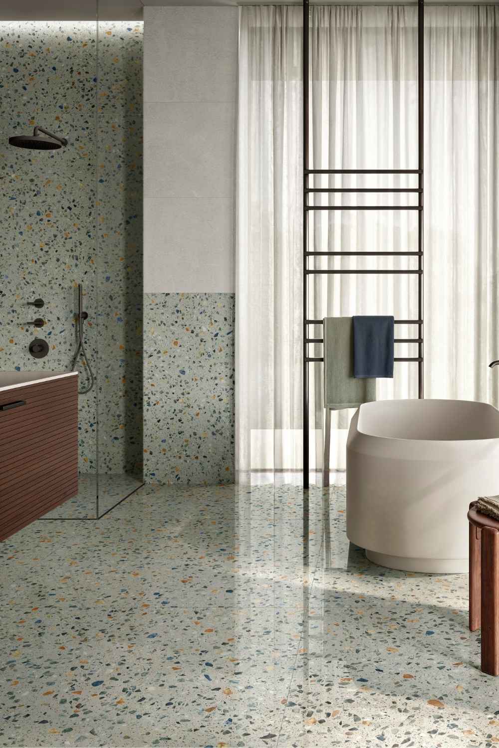 Modernes Badezimmer mit Sant Agostino Glow Plus Sage in glänzend polierter Terrazzo-Optik als Boden- und Wandfliese, mit heller Grundfarbe, bunten Steinfragmenten sowie freistehender Badewanne und bodengleicher Dusche