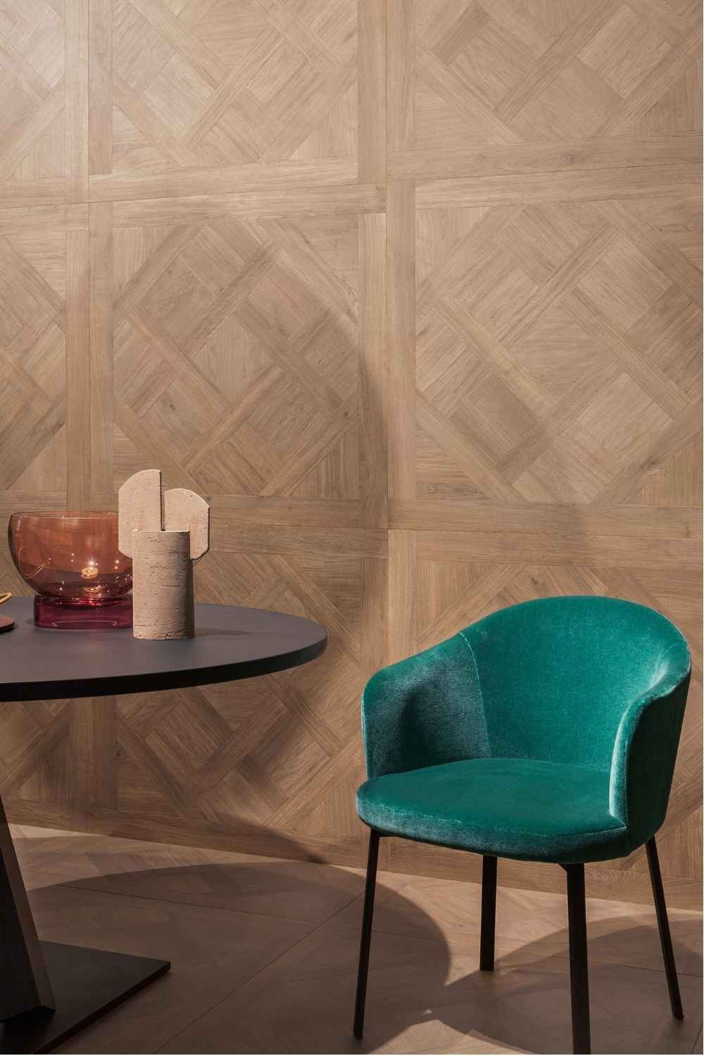 Sant Agostino Ricordi Classic 02 Primewood Nut als Wandfliese in warmer Nussbaum-Holzoptik mit dekorativer Tafelparkett- und Kassettenparkett-Struktur, kombiniert mit grünem Sessel und modernem Tisch