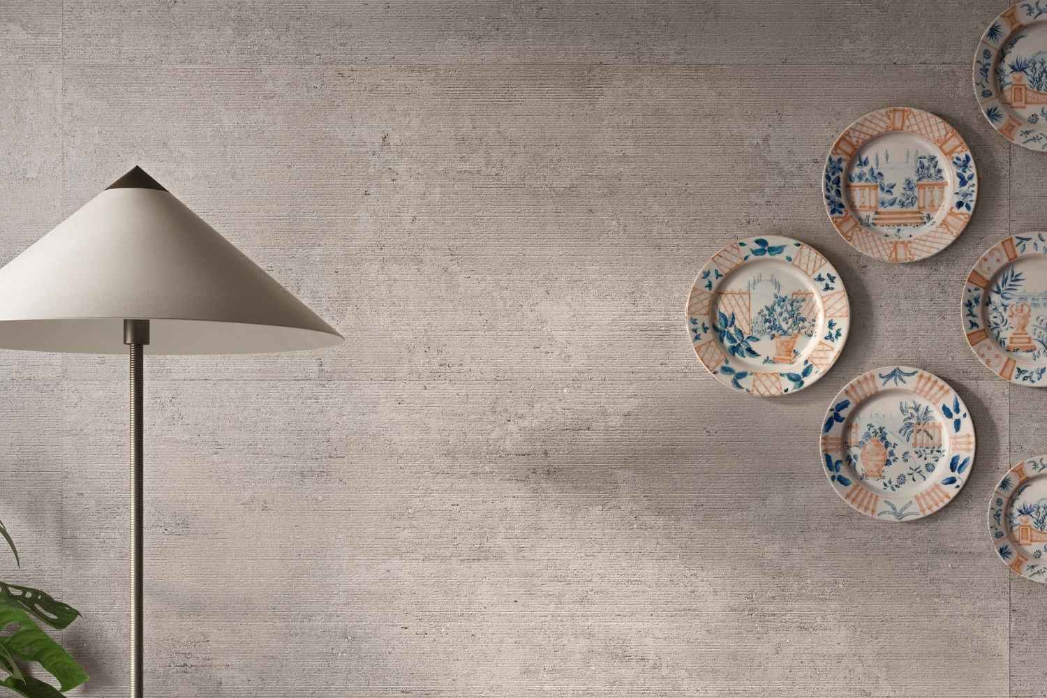 Sant Agostino Glow Concrete als großformatige Wandfliese in grauer Betonoptik mit feiner horizontaler Struktur, dekoriert mit Stehleuchte und Wandtellern
