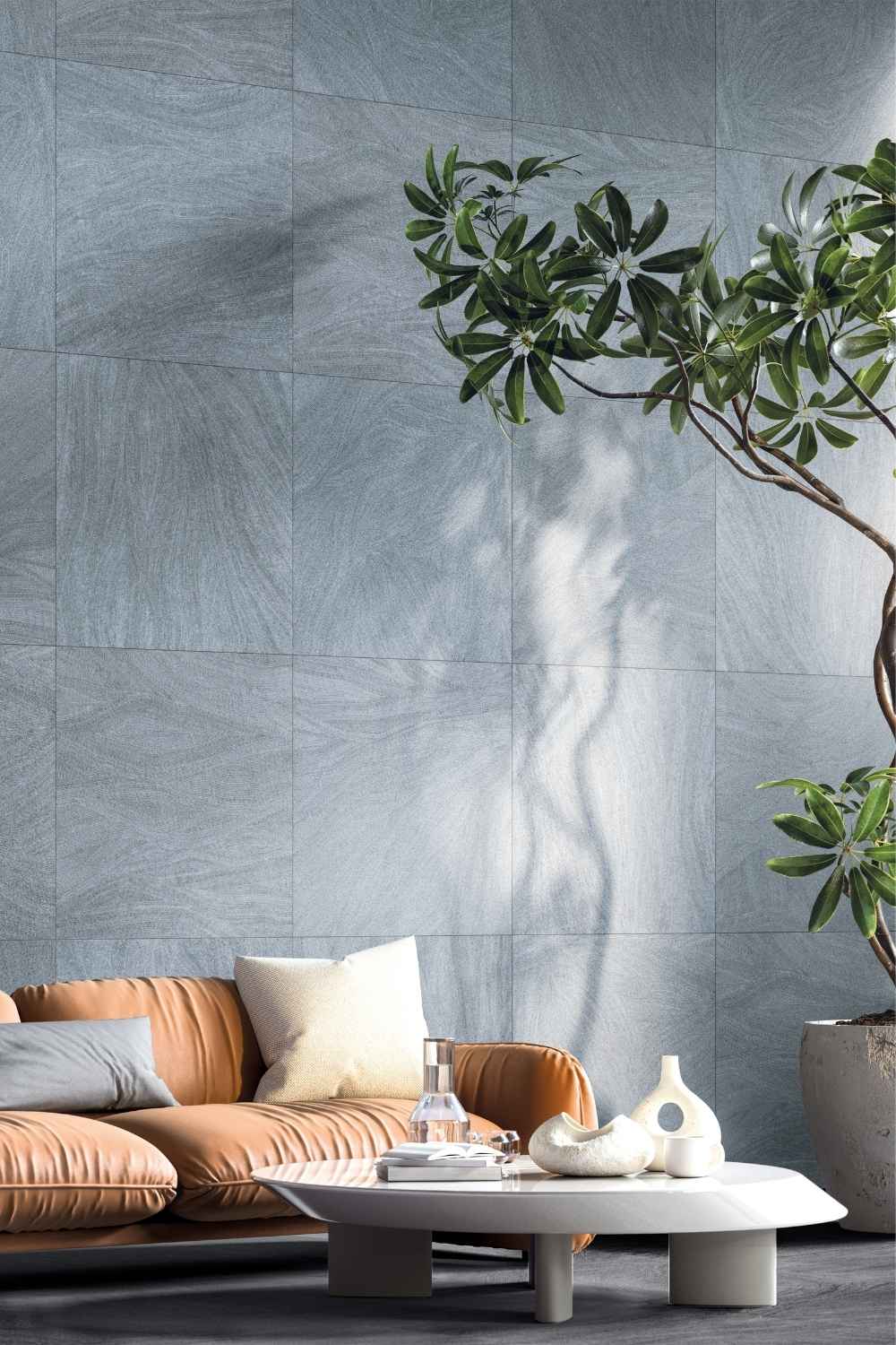 Refin Ink Wavy als Wandfliese in Blau- und Grautönen mit feiner künstlerischer Linienstruktur und sanft geschwungenem Muster in einem modernen Wohnbereich mit Ledersofa und Pflanzen