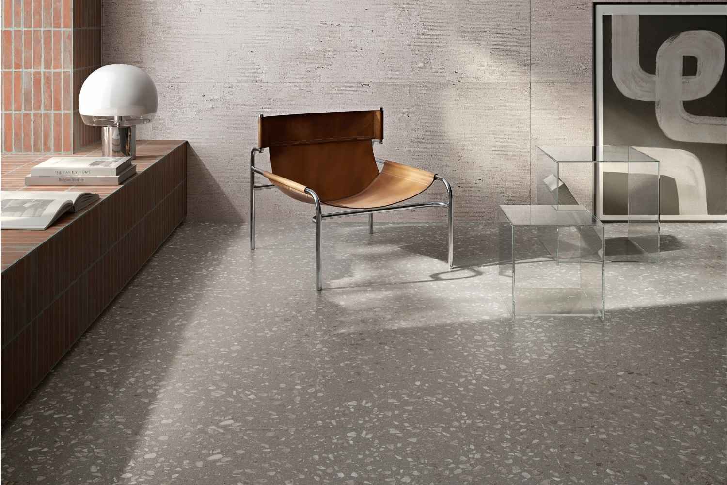 Sant Agostino Glow Grey als graue Bodenfliese in feiner Terrazzo-Optik mit hellen Steinfragmenten, kombiniert mit Lederstuhl, Glastischen und moderner Einrichtung